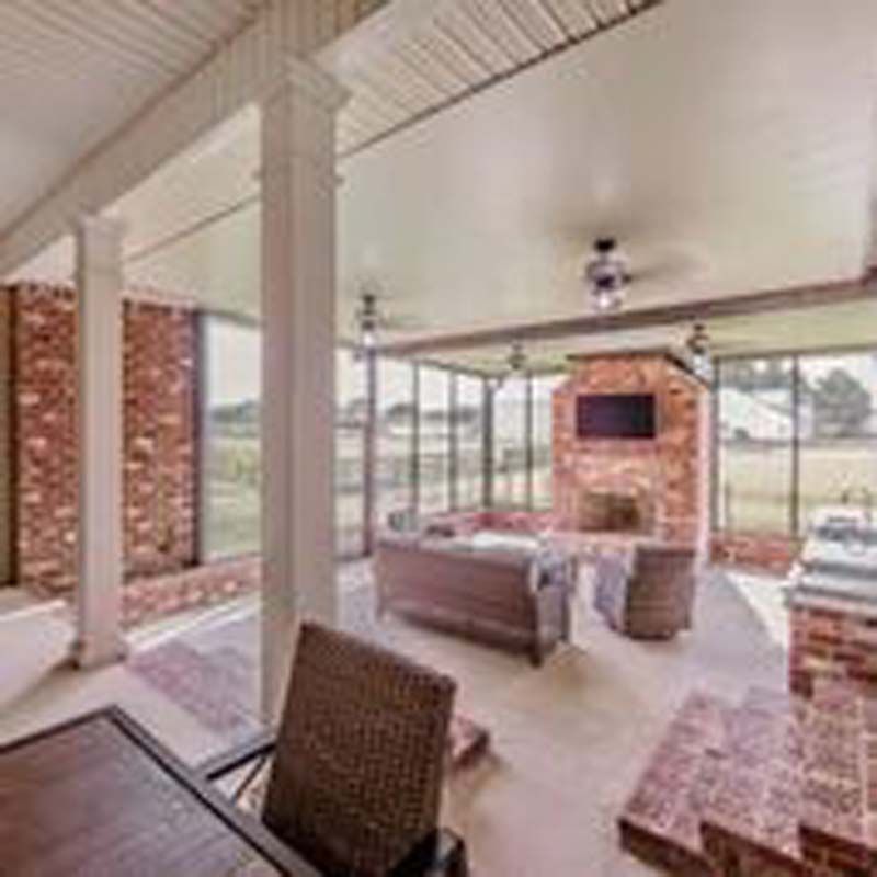 Covered patio with wicker seating, brick fireplace, and large windows overlooking a field