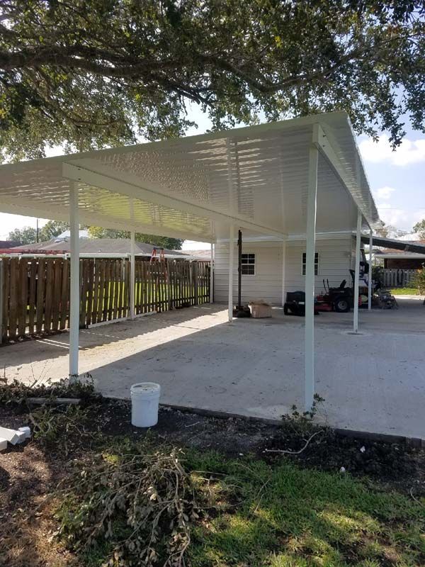 White metal carport with slatted roof over a concrete driveway beside a fenced yard.