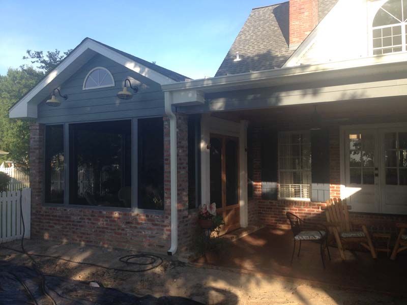 Brick house patio with screened porch, patio furniture, and sunlight casting shadows