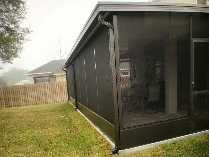 Screened porch on a house with black mesh walls and a grassy backyard, bordered by a wooden fence.