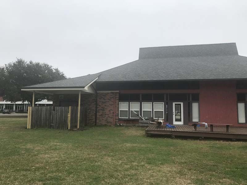 Single-story brick building with a covered entrance and grassy yard under an overcast sky
