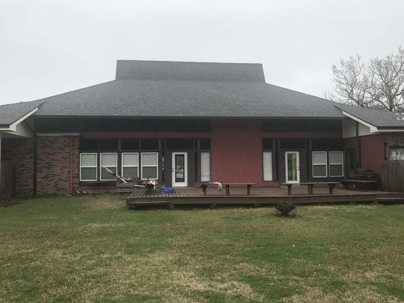 Single-story brick building with a covered porch and grassy front lawn under an overcast sky