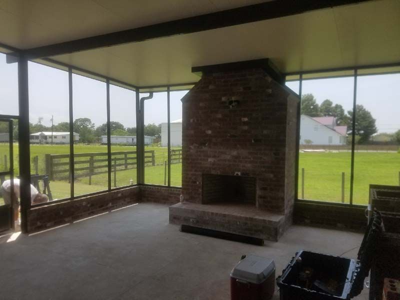 Covered patio with brick fireplace, concrete floor, and glass walls overlooking a grassy yard