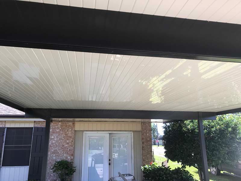 Covered front porch with white paneled ceiling, brick wall, and double glass doors.