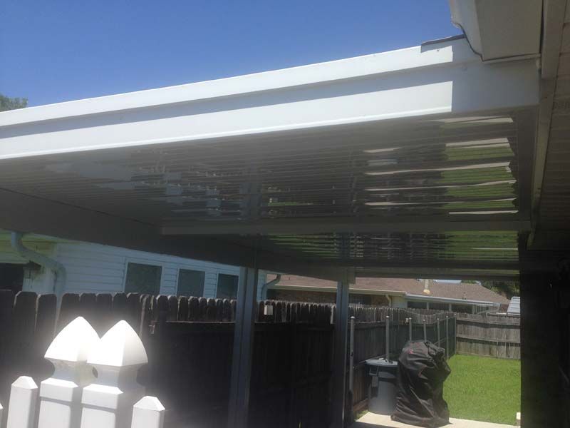 Backyard patio with a corrugated metal roof, fence, and a grill in the shade