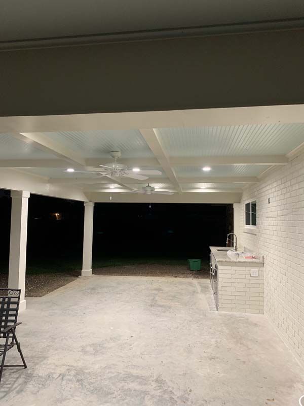 Covered patio at night with white columns, ceiling lights, and an outdoor counter beside a dark yard.