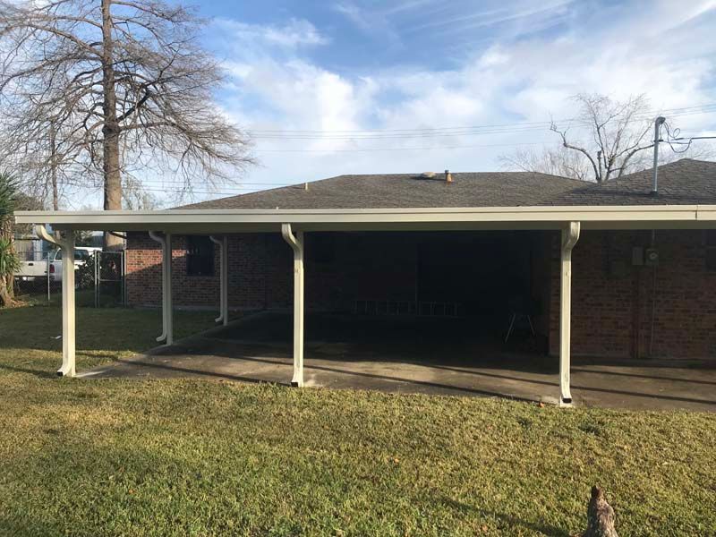 Single-story brick house with a covered carport, white support posts, and a bare tree in front yard
