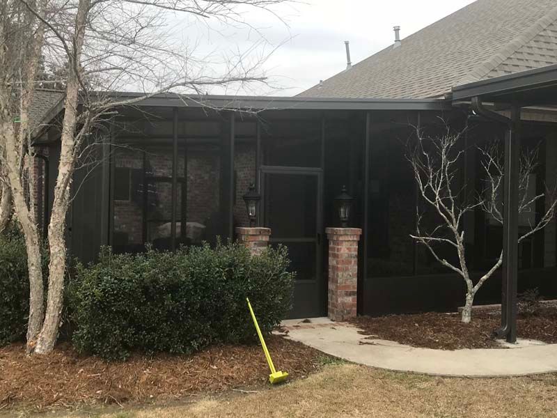 Front porch of a house with brick columns, shrubs, a bare tree, and a yellow shovel in the yard