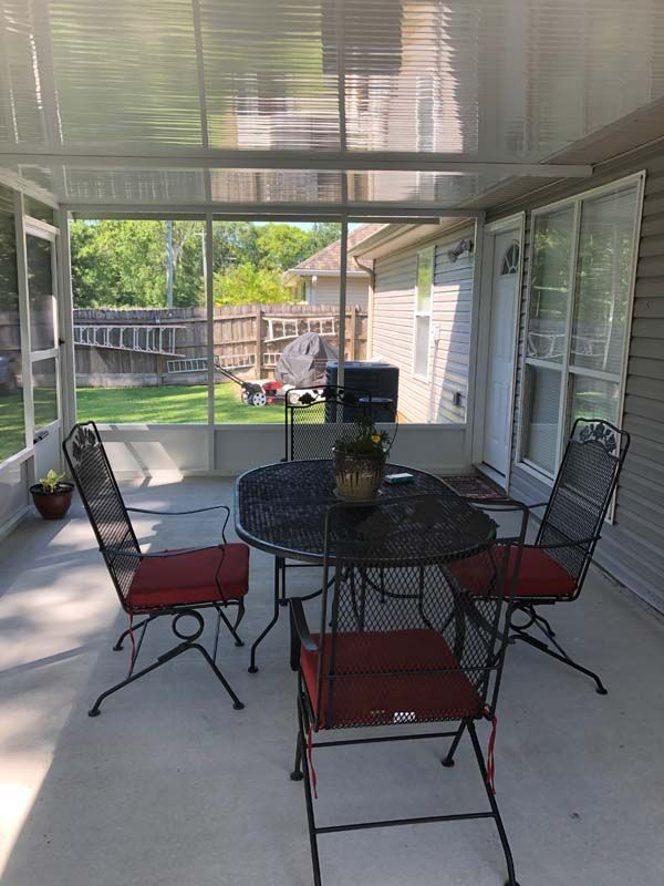 Covered patio with black metal table and chairs, red cushions, and a backyard view beyond the screen.
