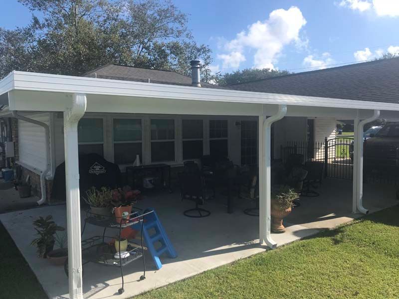 Covered patio with white columns, porch furniture, and a blue step stool beside a house.