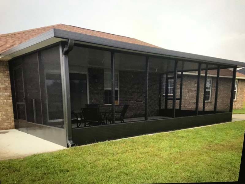 Screened patio attached to a brick house with a grassy lawn.