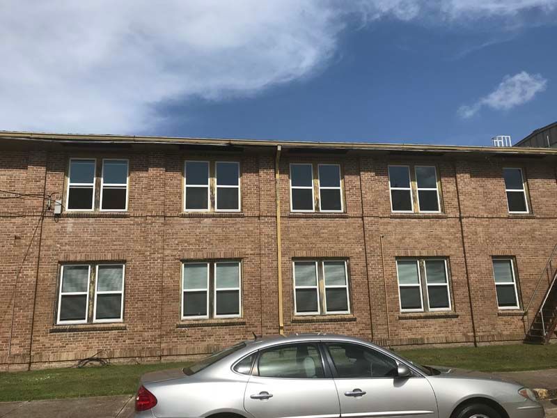 Brick apartment building with many windows behind a silver car under a blue sky