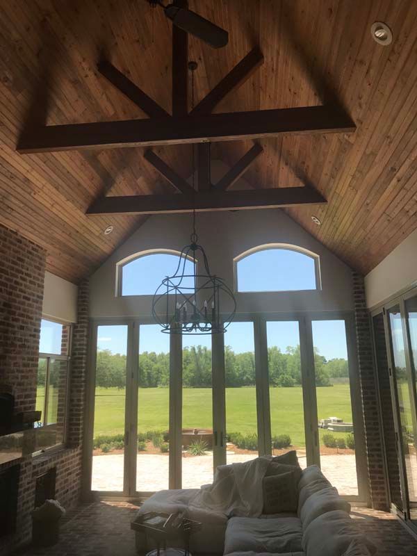 Great room with vaulted wood ceiling, large windows, brick fireplace, and a sofa overlooking a green field.