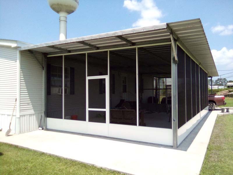 Covered patio attached to a white building with screened windows and a grassy lawn nearby