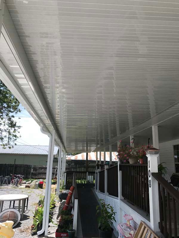 Covered porch with white ceiling, black railing, potted plants, and floral wall art overlooking a yard