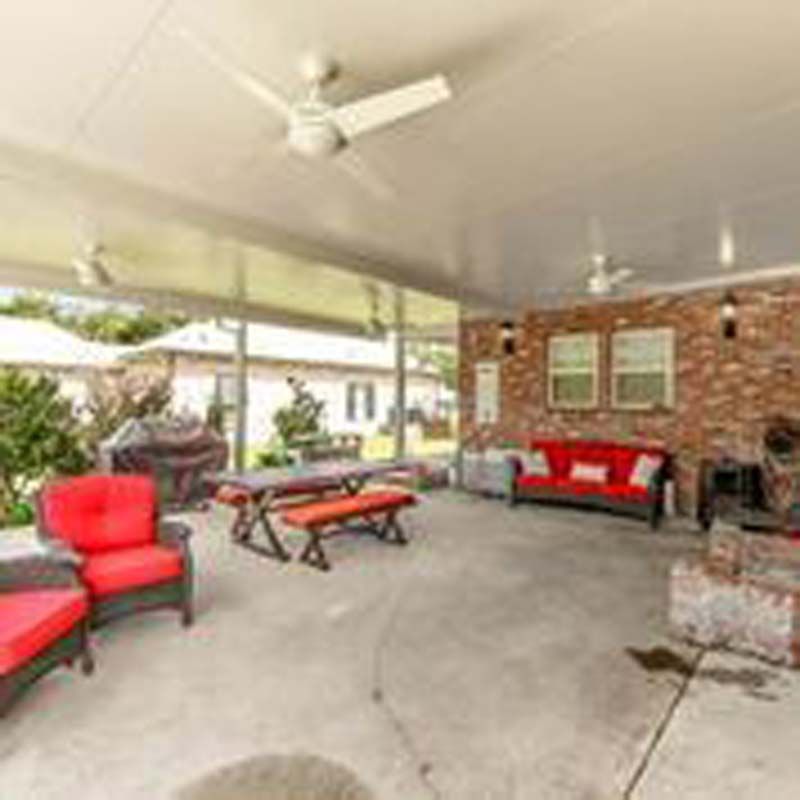 Covered patio with red seating, a picnic table, and brick wall with windows and grill