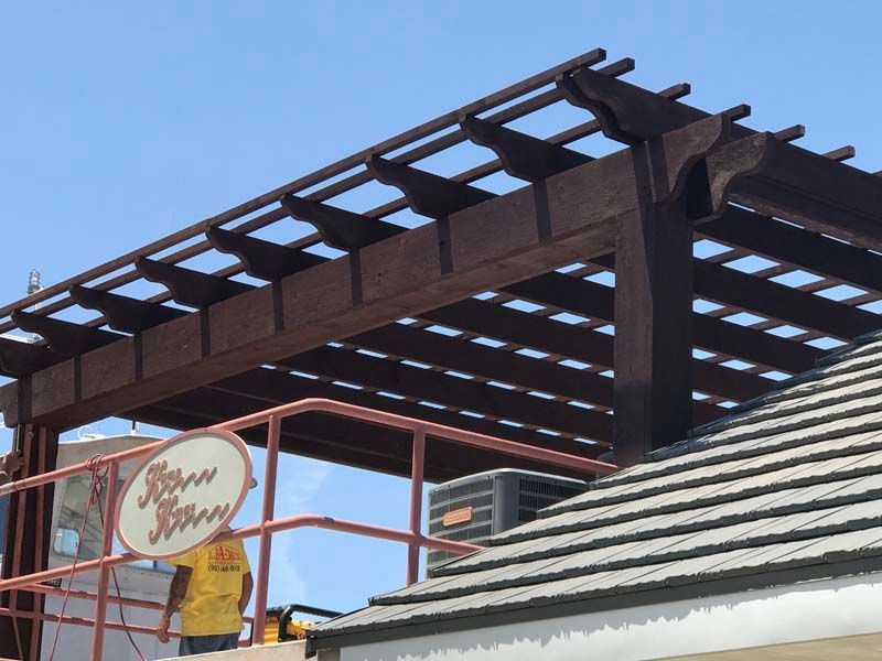 Dark wooden pergola over a building with a tiled roof and a hanging sign outside a storefront