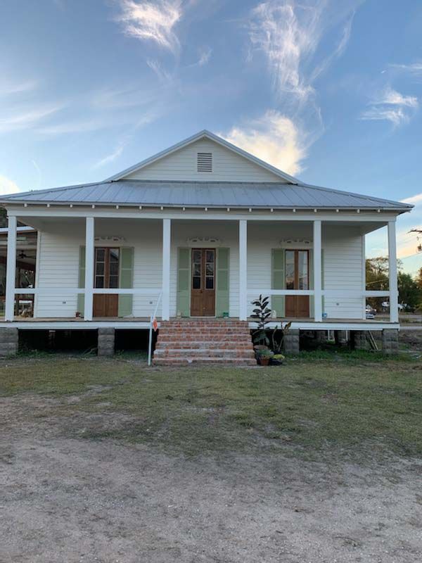 Front porch farmhouse with white columns and brick steps under a blue sky