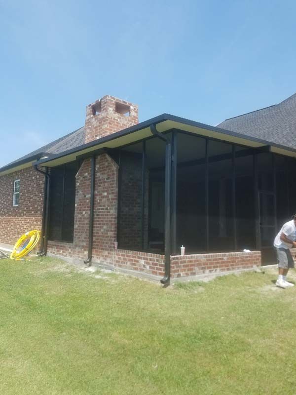 Brick house with screened porch and chimney, green lawn, and a person working at the right edge.
