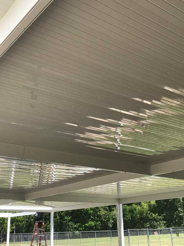 Covered outdoor pavilion roof with sunlight patterns and a chain-link fence below