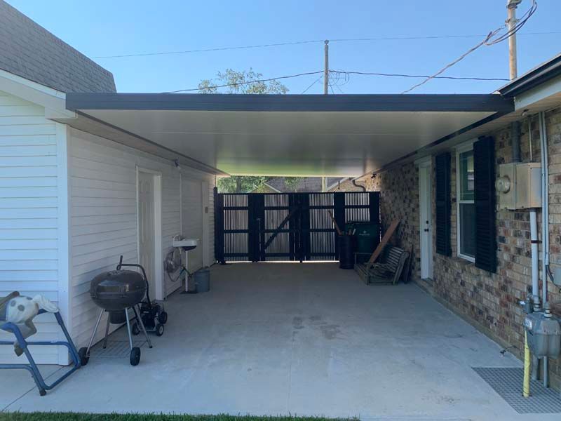 Covered concrete driveway with patio furniture and a gate at the back of a house