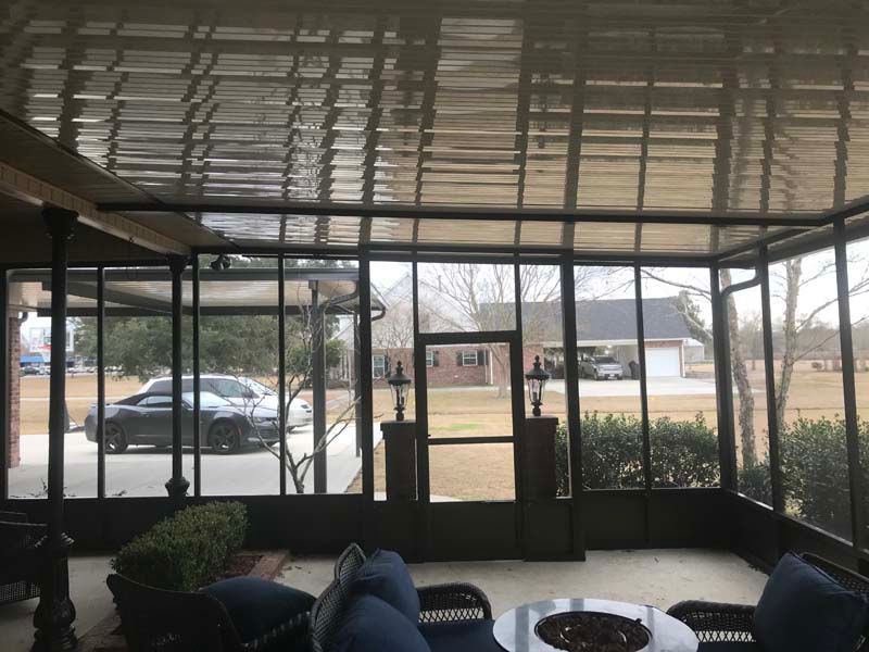 Covered porch with black chairs, potted plants, and glass doors overlooking a yard.