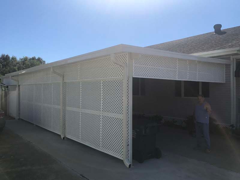 White lattice-enclosed patio attached to a house, with a person standing in the shaded carport area.
