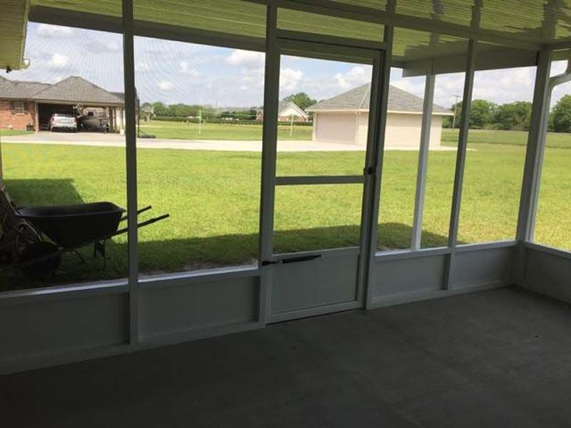 Screened porch overlooking a grassy backyard and neighboring houses, with a chair on the left.