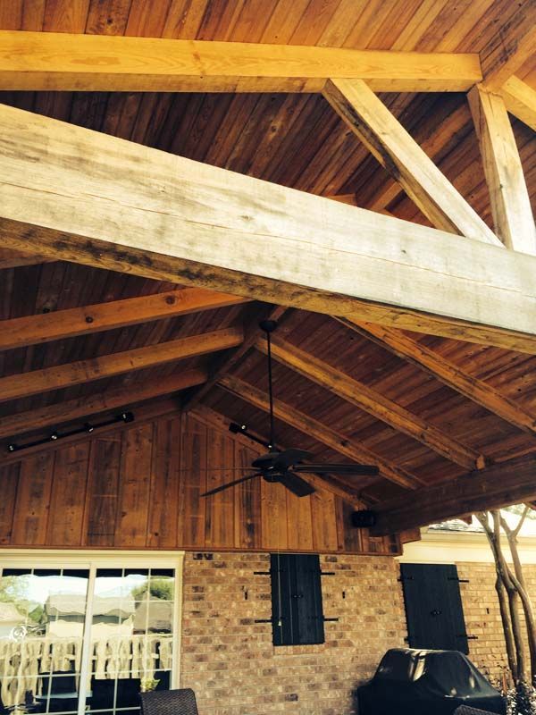 Wooden pavilion ceiling with exposed beams and a brick wall, with a ceiling fan and windows below