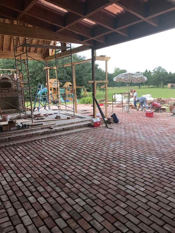 Covered brick patio under construction with metal scaffolding and building materials beside an open grassy field