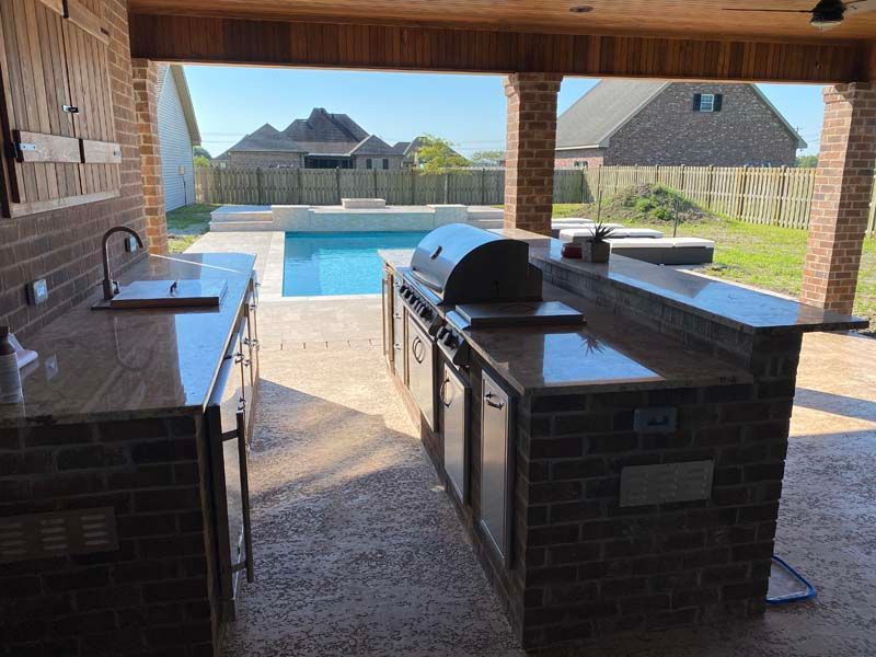 Covered patio with outdoor sink and grill overlooking a backyard pool and neighboring houses