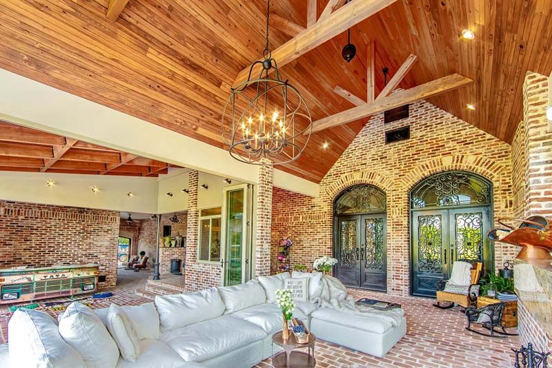 Spacious rustic living room with wood cathedral ceiling, brick walls, chandelier, and white sectional sofas