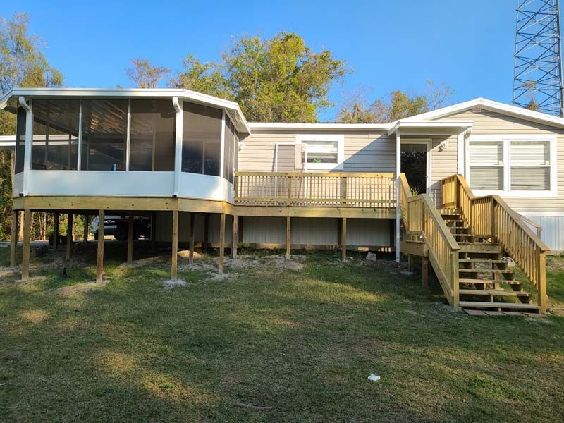 Raised mobile home with screened porch, wooden deck, and stairs in a grassy yard.