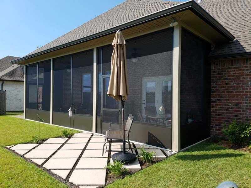 Patio with screened enclosure, patio table and umbrella beside a brick house and lawn.