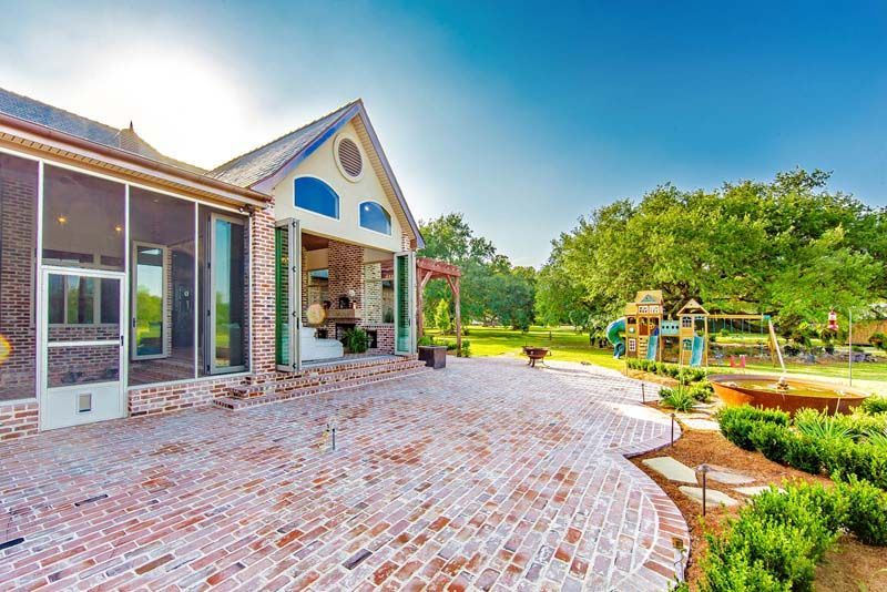 Brick patio leading to a house with a covered entry and landscaped garden in bright sunlight
