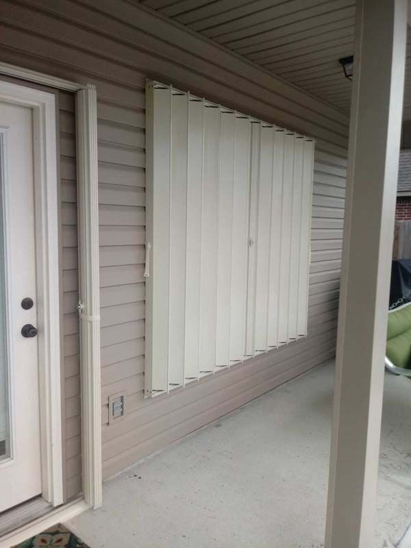 White shutters covering a window on a beige house porch with a door and support column