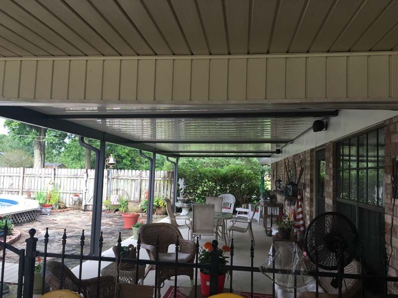 Covered outdoor patio with metal chairs, table, ceiling fan, and potted plants beside a house