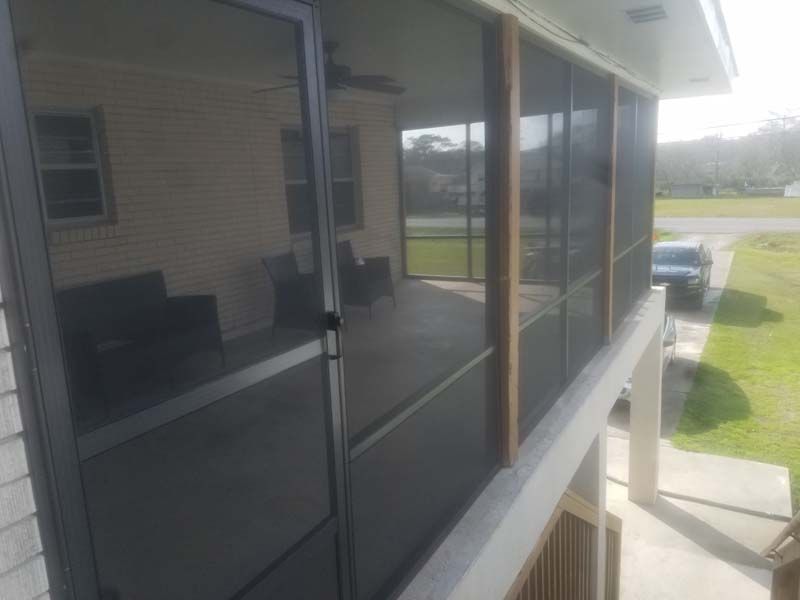 Screened porch beside a house, with dark mesh panels and a view of a grassy yard and driveway.
