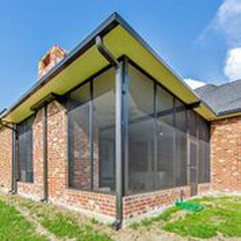 Brick house corner with black-framed glass sunroom and sloped roof under a blue sky