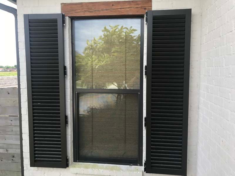 Closed window with black shutters on a white brick wall and wood trim.