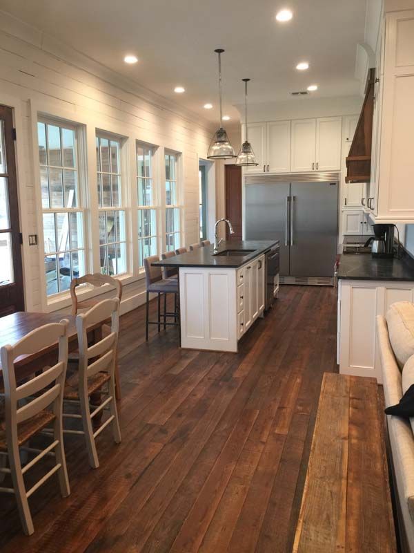 Bright kitchen with island, stainless fridge, white cabinets, wood floors, and large windows along one side