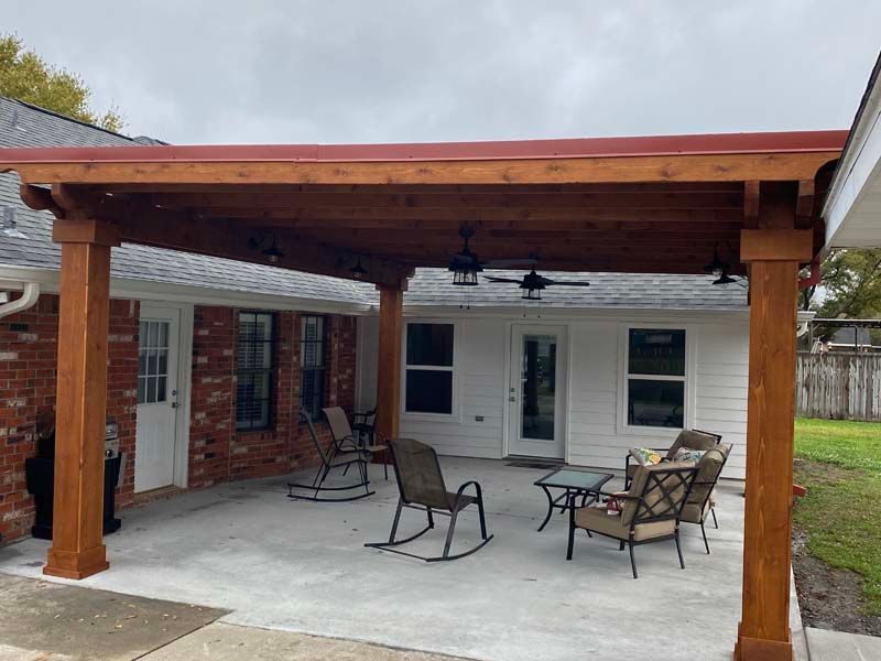 Covered patio with wooden beams, brick house wall, ceiling fan, and outdoor seating on a concrete floor