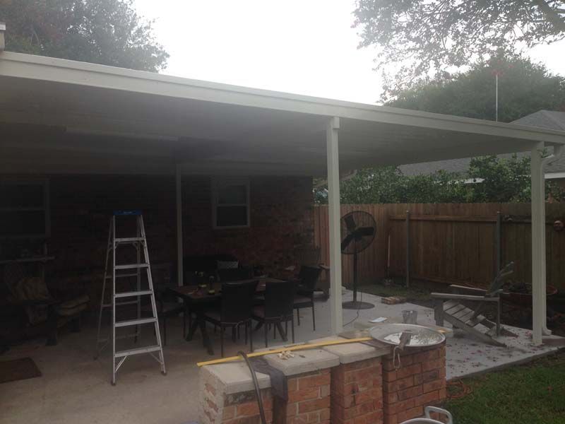 Covered patio with a ladder, outdoor furniture, and stacked bricks in a backyard.