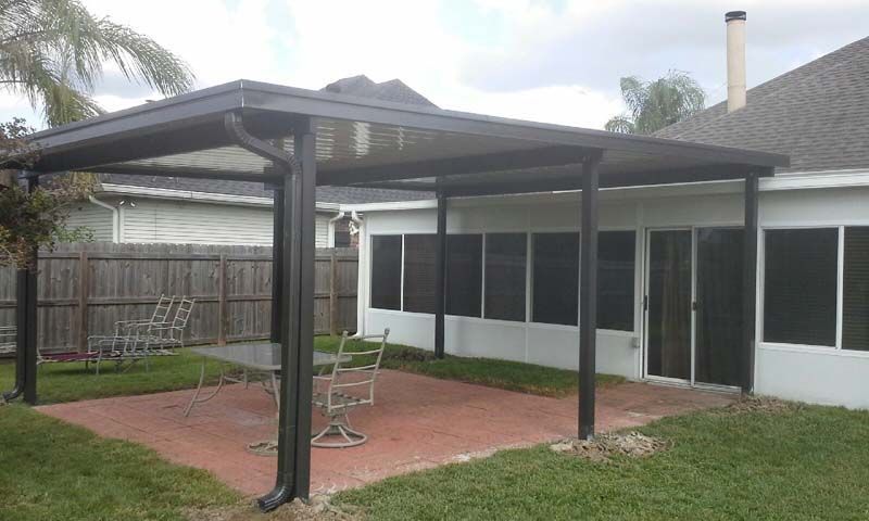 Backyard patio with a dark metal pergola, red pavers, and a screened house wall.