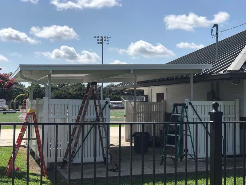 Covered walkway beside a fenced sports area under a bright blue sky