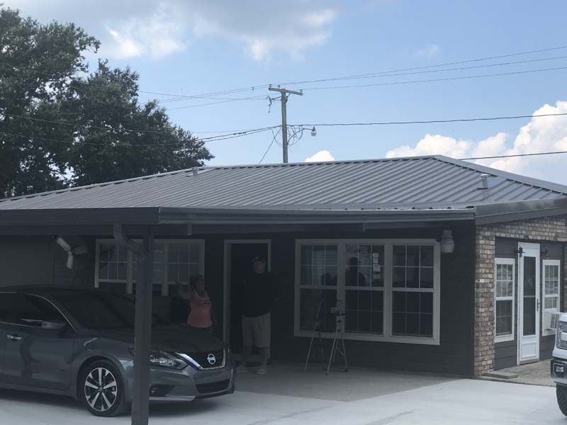 Single-story brick house with a carport, parked car, and front porch under a cloudy sky