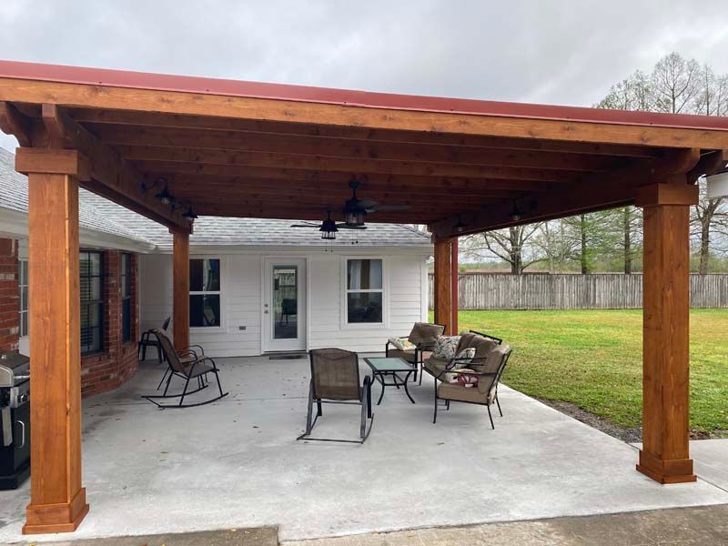 Covered patio with wooden roof, concrete floor, and outdoor chairs beside a house