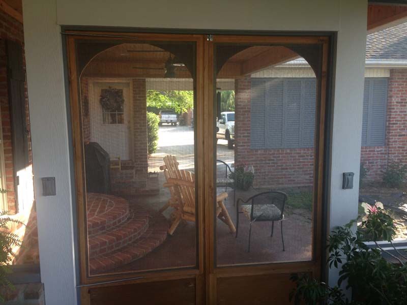 Sliding glass doors opening to a shaded patio with chairs and a potted plant, viewed from a covered porch