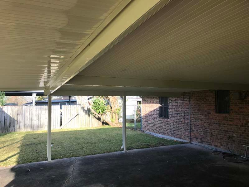 Covered backyard patio with brick wall, lawn, and fence in the background.