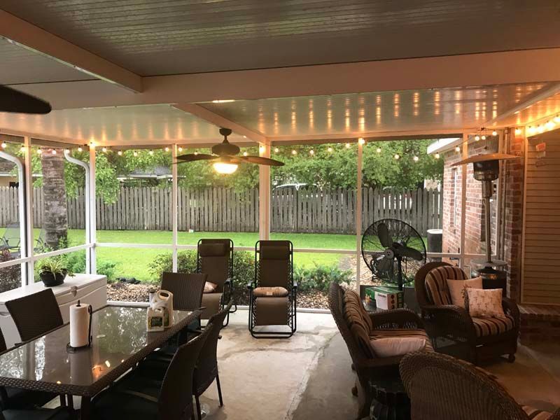 Covered patio with wicker chairs and a dining table overlooking a green backyard and wooden fence.